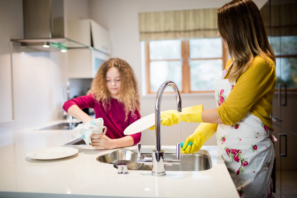 mother assisting daughter in washing plate in kitchen